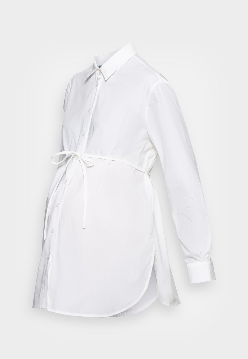 Vit skjorta med långa ärmar, krage, knappfront och ett bälte i midjan. Tillverkad av lättviktsmaterial med en slät textur.