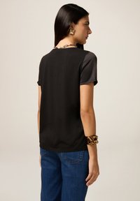 Top nero a maniche corte con texture liscia, caratterizzato da un collo rotondo e un design della schiena uniforme, abbinato a jeans in denim blu.
