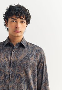 Tumesinise värvusega nööpidega särk, millel on keerukas paisley mustriga kuldsete, oranžide ja türkiissiniste toonidega; kangal on sile tekstuur ja klassikaline krae.