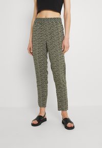 Spodnie w kolorze oliwkowym z wzorem w białe kreski, z elastycznym pasem. Połączone z czarnymi płaskimi sandałami.