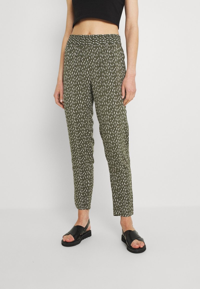 Spodnie w kolorze oliwkowym z wzorem w białe kreski, z elastycznym pasem. Połączone z czarnymi płaskimi sandałami.
