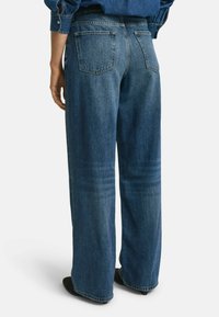 Wijduitlopende blauwe denim jeans met een vervaagde was, met twee achterzakken en een rechte snit, weergegeven vanuit de achterkant met zichtbare stikdetails.