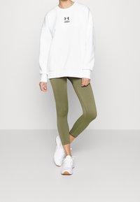 Bílé mikina s logem, olivově zelené legíny a bílé tenisky. Mikina má uvolněný střih a legíny jsou pěkně přiléhavé.