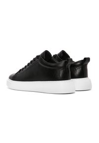 Sneaker in pelle nera con un design elegante, suola in gomma bianca e chiusura con lacci. Presenta una leggera texture e un tallone rinforzato.