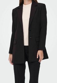 Černý přizpůsobený blazer s klopami, dvěma předními kapsami a zapínáním na jeden knoflík, kombinovaný se svetrem se žebrováním v světlé barvě.