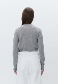 Haut gris à manches longues en matière douce, avec un col rond et des manches ajustées, associé à un pantalon blanc taille haute.