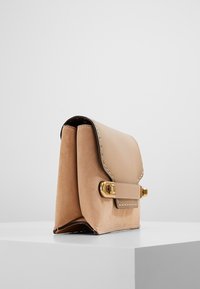 Borsa a tracolla in pelle beige con forma strutturata, cuciture a contrasto e chiusura in metallo dorato. Superfici lisce e testurizzate.