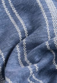 Tissu bleu avec des rayures verticales blanches, montrant une texture tricotée et des plis pour une apparence douce et tissée.