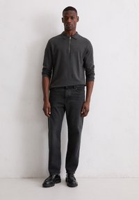 Ciemnoszara, długorękawowa koszulka polo z zamkiem przy kołnierzu, zestawiona z ciemnymi dżinsami i czarnym obuwiem, stojąca na jednolitym tle.