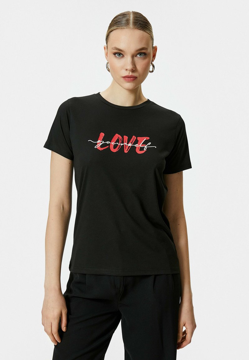 Camiseta negra con texto "LOVE" en rojo y en negrita, con un acento blanco y una textura suave y lisa. Combinada con pantalones negros.