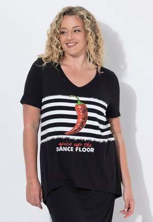 Frau mit lockigen blonden Haaren, die ein schwarzes V-Ausschnitt-Shirt mit weißen Streifen, rotem Chili-Grafik und Text "spice up the dance floor." trägt