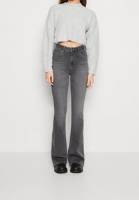 Suéter gris cortado de manga larga, combinado con unos pantalones de mezclilla acampanados grises de cintura alta. La modelo lleva zapatos negros; diseño simple y limpio.