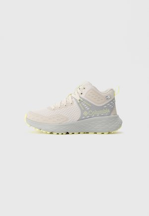 Baskets de sport mid-top de couleur beige clair de Columbia avec une tige en maille, une semelle épaisse et texturée, et des accents jaunes incluant le logo et la tirette.