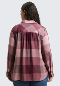 Gekruiste blouse in verschillende tinten roze. Knopmanchetten en een schouderdetail aan de achterkant. Zacht materiaal met een vloeiende, ontspannen pasvorm.