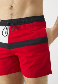 Pantaloni da bagno rossi con un design a pannelli in bianco e nero, vita elastica con cordoncino e tessuto morbido e leggero.