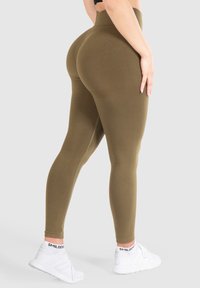 Leggings verdi oliva a vita alta realizzati in materiale elasticizzato, con una texture liscia e un design aderente, abbinati a sneakers bianche.