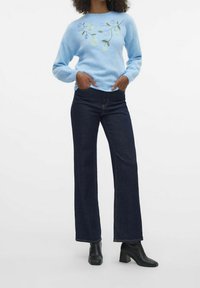 Light blue knitted sweater featuring floral embroidery on the front, paired with dark wash flared jeans and black heeled ankle boots.