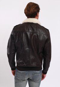 Brown leather bomber jacket with a white shearling collar, ribbed cuffs, and hem. Features shoulder epaulets and a patch on the sleeve.