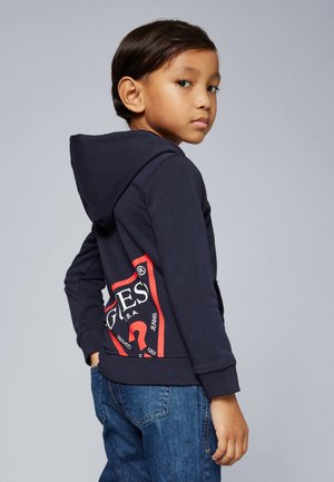 Haut à capuche bleu marine avec un logo graphique rouge au dos, associé à un jean bleu. Tissu doux, design décontracté et poche kangourou à l'avant.