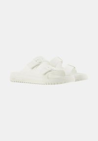 Sandalias blancas sin hebillas con dos correas ajustables, hechas de material suave. Suela con relieve para mayor agarre. Diseño minimalista con forma redondeada.