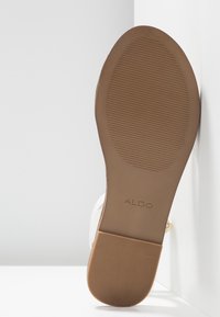 Semelle d’une chaussure plate marron avec grip texturé, nom de marque ALDO visible, positionnée verticalement sur fond blanc.