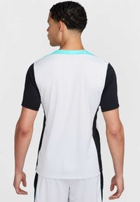 Camiseta deportiva de manga corta con un frente blanco, laterales negros y un cuello turquesa. Confeccionada en tejido ligero y transpirable.