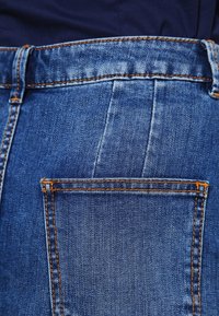 Pantalones vaqueros de mezclilla azules con un bolsillo trasero con costura naranja y una textura suave, que muestran un ajuste y diseño clásicos.