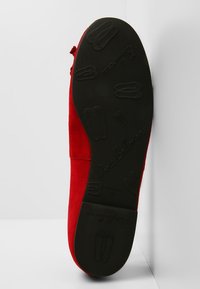 Chaussure en daim rouge montrée de la semelle avec une semelle extérieure en caoutchouc noir présentant des motifs de chaussure embossés et la marque "Pretty Ballerinas".