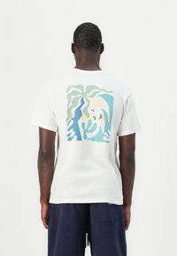 White cotton t-shirt featuring a colorful abstract design in blue, green, and yellow on the back. Short sleeves and a crew neck.