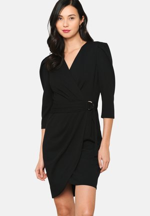 Robe noire à manches trois-quarts, avec un décolleté en V profond et une ceinture en ton doré accentuée à la taille. Tissu texturé et design ajusté.