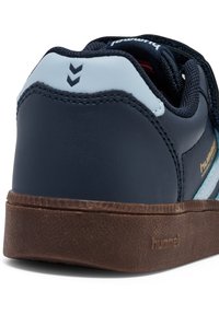 Dunkelblaue Sneaker mit einer strukturierten Gummisohle, hellblauen Akzenten, goldenen Logo und Chevron-Muster auf der Rückseite. Obermaterial aus Synthetik.