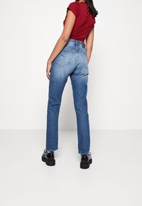 Blue denim jeans with a straight leg cut, high waist, and back pockets, paired with black shoes, shown from a rear view.