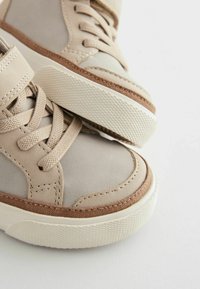 Beige sneakers med en mix av texturerad läder och mocka, med gummisula, snörning och vadderad vrist för komfort.