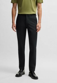 Black trousers with a slim fit, featuring a smooth texture, a front zipper, and button closure. Worn with a green short-sleeve shirt.