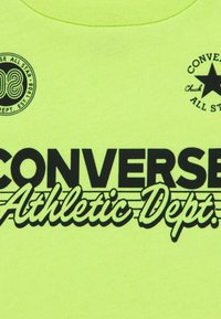 Μπλουζάκι από βαμβάκι σε νέον κίτρινο χρώμα με μαύρα γραφικά κείμενα "CONVERSE Athletic Dept." και λογότυπα. Λείο υλικό με σχέδιο λαιμού τύπου crew neck.