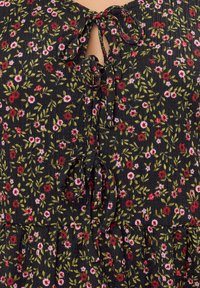 Schwarzer Stoff mit floralem Muster in Rot und Rosa, mit einem Schlüssellochausschnitt, der mit Schleifen gebunden ist. Strukturierte Oberfläche mit gerippter Verarbeitung.