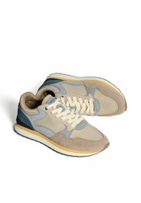 Zapatillas deportivas en color beige y gris, con materiales de ante y malla, cordones claros, acentos naranjas y suela de goma. Punta redondeada y diseño acolchado.