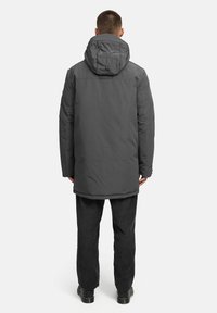 Garšs pelēks pūkains mētelis ar kapuci, ar gludu tekstūru un taisnu griezumu, kas beidzas zem gurniem. Uzvilkts kopā ar melniem korduroja biksēm.