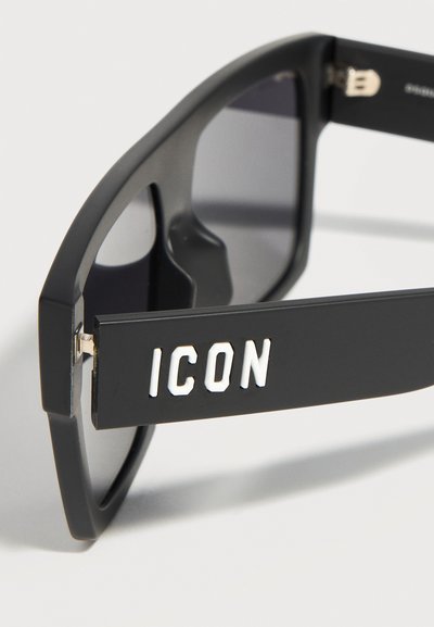 Μαύρα ορθογώνια γυαλιά ηλίου με σκουρόχρωμους φακούς και την επιγραφή «ICON» σε λευκό, σκαλισμένη στο πλαϊνό μπράτσο.
