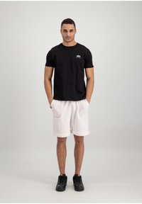 T-shirt en coton noir avec un logo sur la poitrine, associé à un short en tricot beige clair avec des revers. Des baskets noires complètent le look.