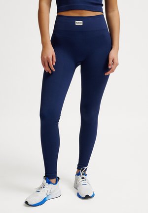 Blå ribstrikkede leggings med høj talje og logopatch, kombineret med hvide og blå sportssko. Glat tekstur og tætsiddende pasform.