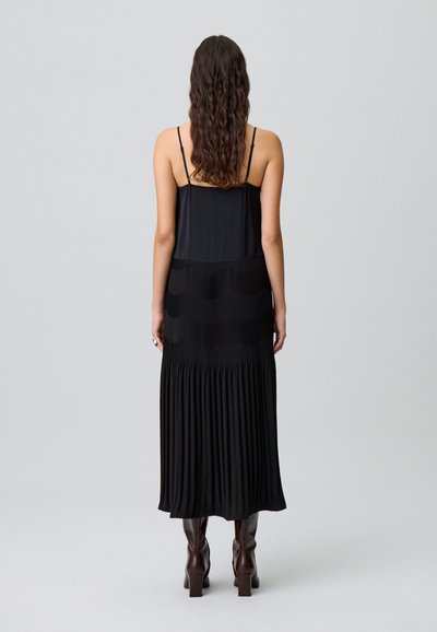 Vestito lungo nero con spalline sottili regolabili, caratterizzato da una texture plissettata all'orlo, sezione superiore liscia e silhouette fluente.