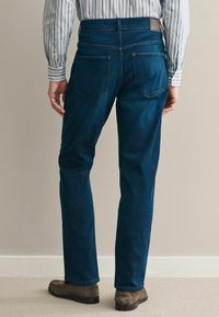 Donkerblauwe spijkerbroek met een rechte pijp, vijf zakken en een leren label op de achterste tailleband. Zachte, gladde textuur.
