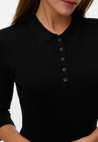 Polo shirt nero a coste con colletto e chiusura a cinque bottoni. Presenta maniche tre quarti e un design aderente.