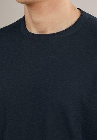 Mörk marinblå T-shirt i mjukt, texturerat tyg med rundad halsringning, som visar subtila sömnadsdetaljer längs kanterna.