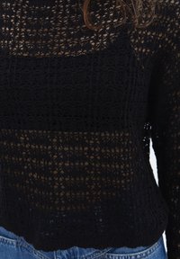 Svart virkad tröja med öppen väv, med ett texturerat mönster och en kortad design. nederkanten är ribbad, vilket kompletterar en avslappnad look.