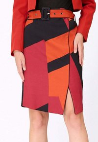 Jupe crayon courte dans des motifs géométriques rouge, orange et noir, avec une fente sur le côté et une ceinture assortie avec une boucle rectangulaire.