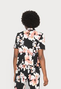 Top peplum preto com flores, de mangas curtas, apresentando padrões de flores em rosa e branco, um recorte nas costas e um design de gola com babados.