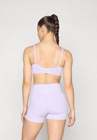 Lilaf sports-bh og shorts laget av elastisk stoff, med justerbare stropper, en glatt tekstur og en logo på baksiden.