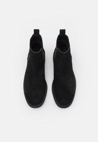 Botas Chelsea de ante negro con una textura suave, paneles laterales elásticos y una tira para facilitar su uso. Suela de goma plana con costuras discretas.